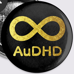 A pin reading AuDHD under an infinity symbol, both filled in with a gold foil texture, on a black background.